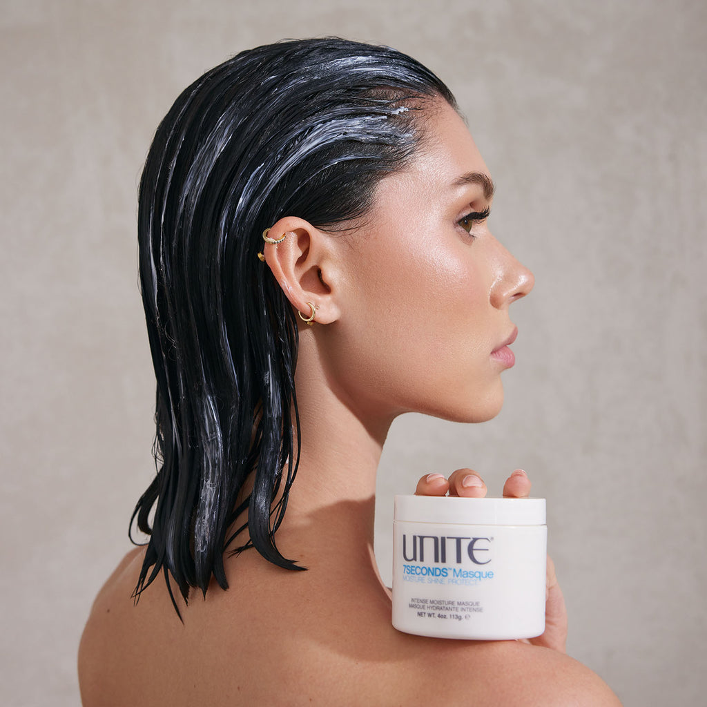 Woman with wet hair wearing hair mask treatment, holding a jar of UNITE Hair 7SECONDS Masque.